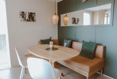 Coin repas confortable dans un logement glamping avec table ovale, banquette, coussins verts et décor nature.