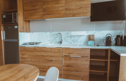 Cocina moderna de glamping con armarios de madera, estufa de gas, fregadero, televisor y cafetera.