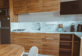 Cocina moderna de glamping con armarios de madera, estufa de gas, fregadero, televisor y cafetera.