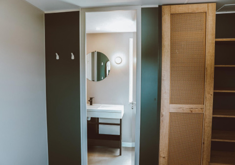 Moderne badeværelse og opbevaring med træskabe og spejl i et luksuriøst glamping-ophold.