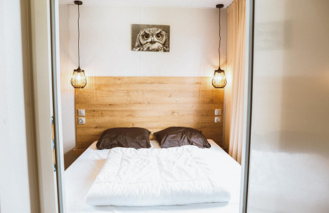 Chambre glamping avec lit double, tête de lit en bois, suspensions modernes et tableau de hibou mural.