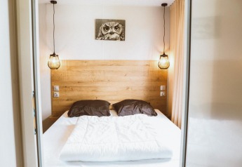 Dormitorio glamping acogedor con cama doble, cabecera de madera, luces colgantes y cuadro de búho.