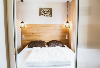 Cozy glamping bedroom with a double bed, wooden headboard, hanging lights, and an owl picture above.