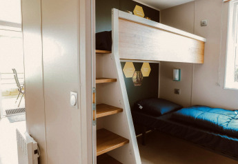 A stylish glamping room featuring a bunk bed with wooden steps and natural light coming from the window.