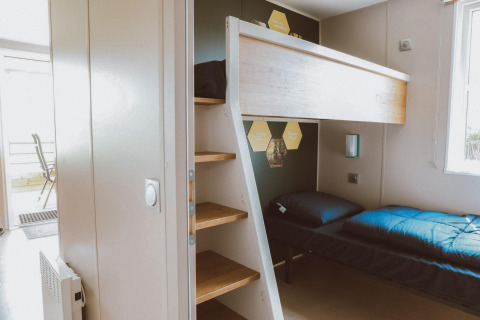 Habitación de glamping moderna con litera, escalera de madera y luz natural entrando por la ventana.