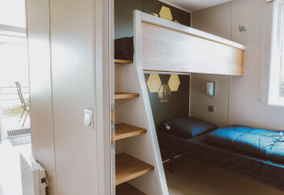 Habitación de glamping moderna con litera, escalera de madera y luz natural entrando por la ventana.