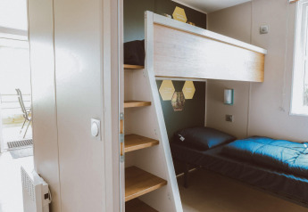 Modernes Glamping-Zimmer mit Etagenbett, Holztreppe und viel Tageslicht durch ein Fenster daneben.