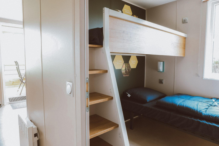 Modernes Glamping-Zimmer mit Etagenbett, Holztreppe und viel Tageslicht durch ein Fenster daneben.