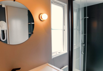 Bagno moderno in Tiny Lodge con specchio rotondo, doccia e finestra al Holiday Park De Boshoek, Paesi Bassi.