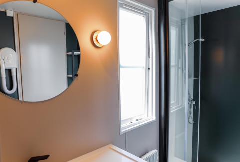 Moderne badkamer in Tiny Lodge met ronde spiegel, douche en raam bij Holiday Park De Boshoek, Nederland.
