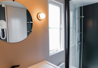 Moderne badkamer in Tiny Lodge met ronde spiegel, douche en raam bij Holiday Park De Boshoek, Nederland.