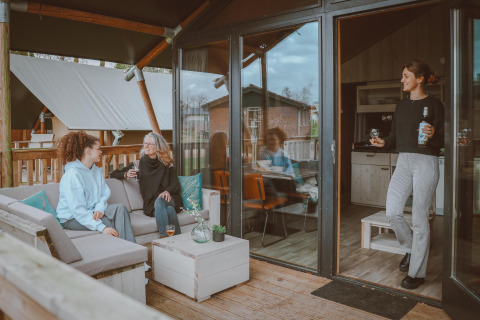 Tres mujeres conversan y disfrutan bebidas en la terraza y dentro de una Tiny Safari House en De Boshoek, Holanda.