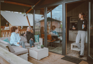 Tres mujeres conversan y disfrutan bebidas en la terraza y dentro de una Tiny Safari House en De Boshoek, Holanda.