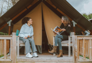 Twee vrouwen zitten voor een Tiny Safari House safaritent op Vakantiepark De Boshoek in Nederland te praten.