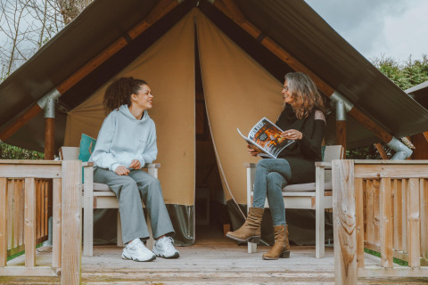 Zwei Frauen sitzen vor einem Tiny Safari House Safarizelt im Ferienpark De Boshoek in den Niederlanden.