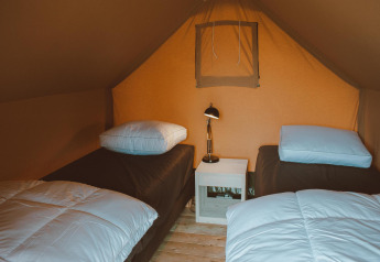 To enkeltsenge med hvide dyner og et natbord i mellem, inde i et safari-telt ved De Boshoek, Nederlandene.