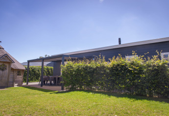 Buitenfoto van Veluwelodge XL bij Vakantiepark De Boshoek in Nederland, met zonnig weer en groene tuin.