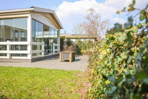 Buitenaanzicht van Veluwe Lounge, lodge in Holiday park De Boshoek in Nederland, met glas, terras en haag.