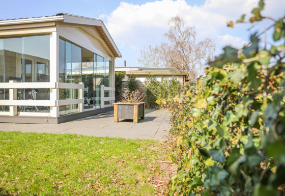 Buitenaanzicht van Veluwe Lounge, lodge in Holiday park De Boshoek in Nederland, met glas, terras en haag.