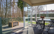 Terraza cubierta en Veluwe Lounge, Holiday park De Boshoek, Países Bajos, con paredes de vidrio y vista al bosque.