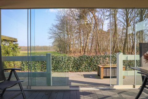 Vue depuis Veluwe Lounge au Holiday park De Boshoek aux Pays-Bas avec grandes baies vitrées, terrasse et arbres.