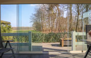 Blick von der Veluwe Lounge im Ferienpark De Boshoek in den Niederlanden: Glasfront, Terrasse und Natur.