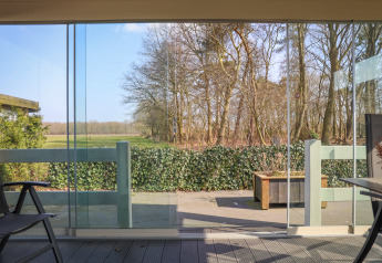 Zicht vanuit Veluwe Lounge in Holiday park De Boshoek Nederland met glazen deuren, terras en bomen buiten.