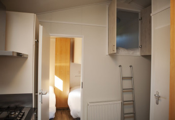 Innenraum der Veluwe Lounge im Ferienpark De Boshoek mit Schlafzimmer, Küche und Hochbett mit Leiter.