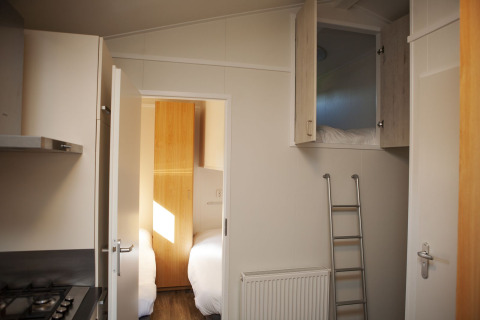 Interieur van Veluwe Lounge bij Holiday park De Boshoek met slaapkamer, keuken en slaapzolder met ladder.