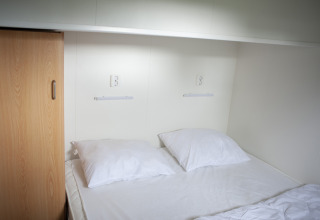 Slaapgedeelte met tweepersoonsbed, witte kussens, kast en stopcontacten bij Veluwe Lounge, De Boshoek.