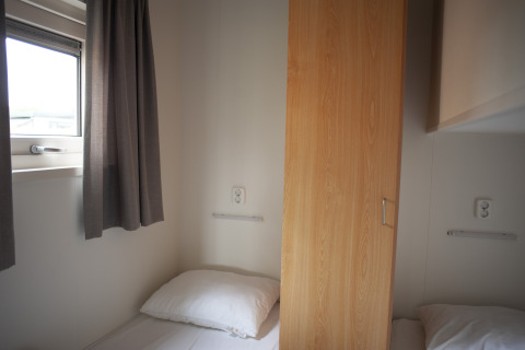 Dos camas individuales separadas por un armario en Veluwe Lounge, Holiday park De Boshoek, Países Bajos.