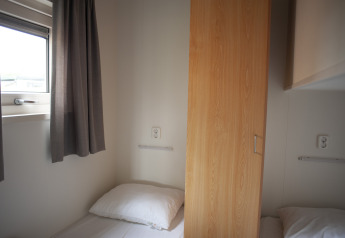 Two single beds separated by a wooden wardrobe in Veluwe Lounge at De Boshoek Holiday Park, Netherlands.
