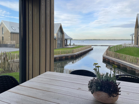 Uitzicht vanuit Villa Oesterdam Royal bij Oesterdam Resort in Nederland met water, huisjes en plant op tafel.