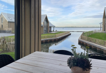 Vista desde Villa Oesterdam Royal en Oesterdam Resort, Países Bajos, con agua, cabañas y una planta en la mesa.