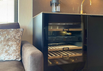 Moderne tekøkken med vinkøleskab, guldvandhane og sofa i en lille villa på Oesterdam Resort, Holland.