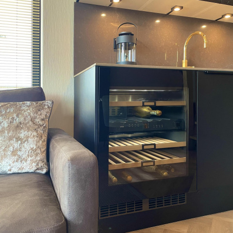 Cocina moderna con vinoteca, grifo dorado y sofá en una casa pequeña del Oesterdam Resort, Países Bajos.