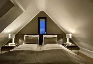 Gezellige slaapkamer in Villa Oesterdam Royal, Oesterdam Resort, Nederland, met dubbel bed en schuin plafond.