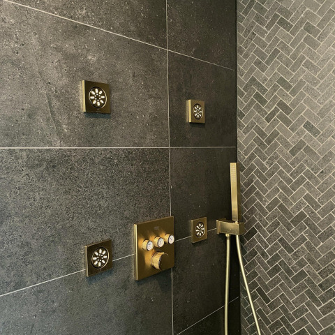 Moderne douche met gouden jets en donkere tegels in een tiny house bij Oesterdam Resort Nederland.
