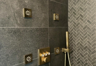 Moderne douche met gouden jets en donkere tegels in een tiny house bij Oesterdam Resort Nederland.
