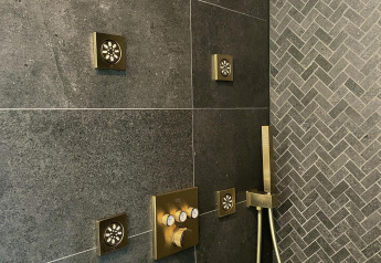 Moderne douche met meerdere messing jets en donkere tegels in een tiny house bij Oesterdam Resort.