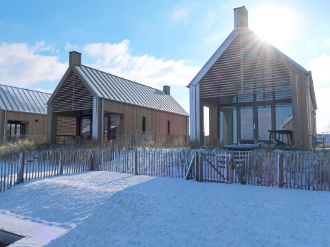 Dos casas pequeñas y modernas con grandes ventanales y nieve en el frente en Oesterdam Resort, Países Bajos.