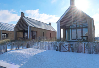 Zwei moderne Tiny Houses mit großen Fenstern und verschneitem Vorgarten im Oesterdam Resort, Niederlande.