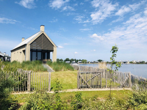 Modern tiny house Villa Oesterdam by the water at Oesterdam Resort, surrounded by greenery and blue sky.