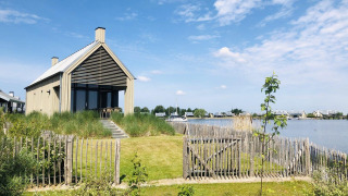 Moderne tiny house Villa Oesterdam aan het water bij Oesterdam Resort, omringd door groen en blauwe lucht.
