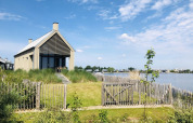 Moderne tiny house Villa Oesterdam aan het water bij Oesterdam Resort, omringd door groen en blauwe lucht.