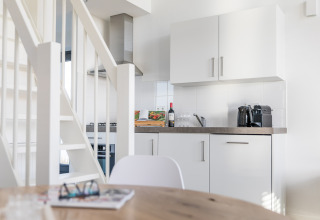 Modern, compact villa kitchen with white cabinets, countertop, and stairs in Villa Oesterdam, Oesterdam Resort, Netherlands.