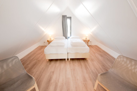 Dormitorio en Villa Oesterdam con dos camas individuales, paredes blancas y suelo de madera, en Oesterdam Resort.