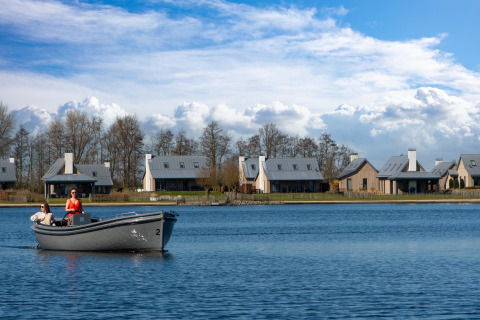 Two women boating on a lake in front of modern villas at Oesterdam Resort, under a blue sky in the Netherlands.