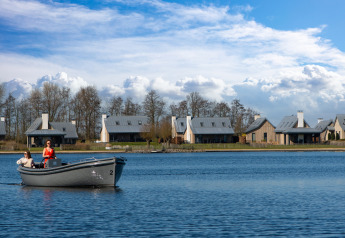 Zwei Frauen fahren mit einem Boot auf einem See vor modernen Villen im Oesterdam Resort in den Niederlanden.