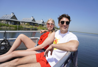 A couple relaxes on a boat in front of Villa Oesterdam tiny house at Oesterdam Resort in the Netherlands.